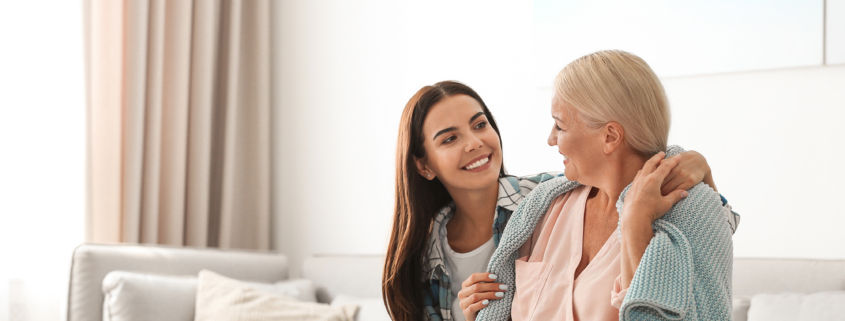 Female caregiver covers older woman on the couch with a blanket