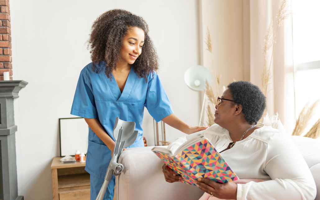 Female caregiver talks to older woman on the couch with a book