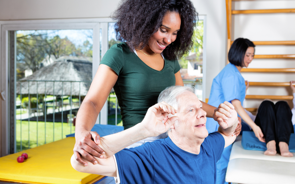 Female caregiver helping an older man through physical therapy