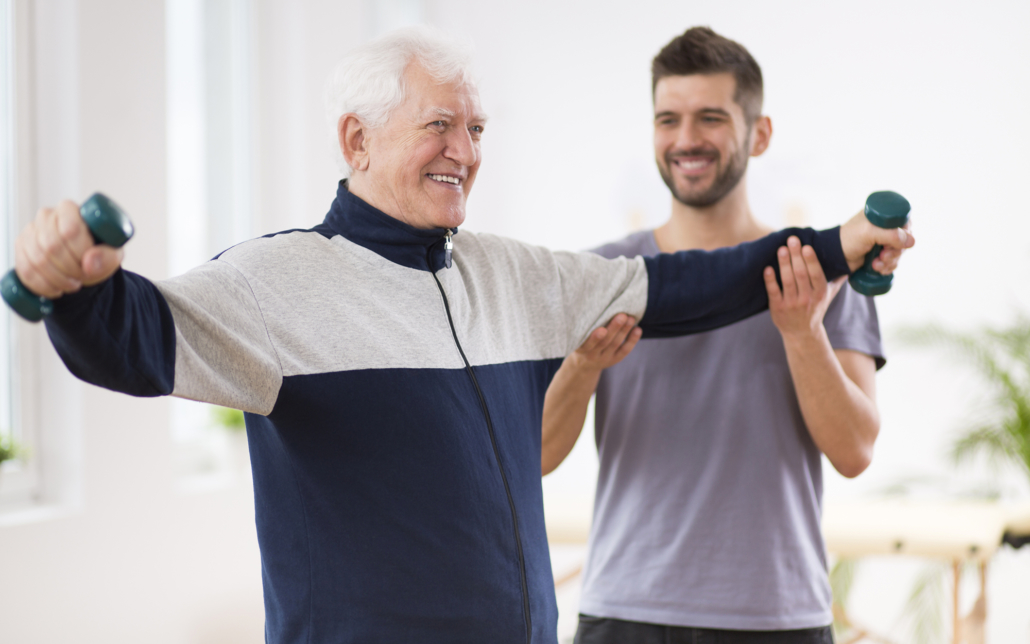 Male caregiver helps older man lift weights