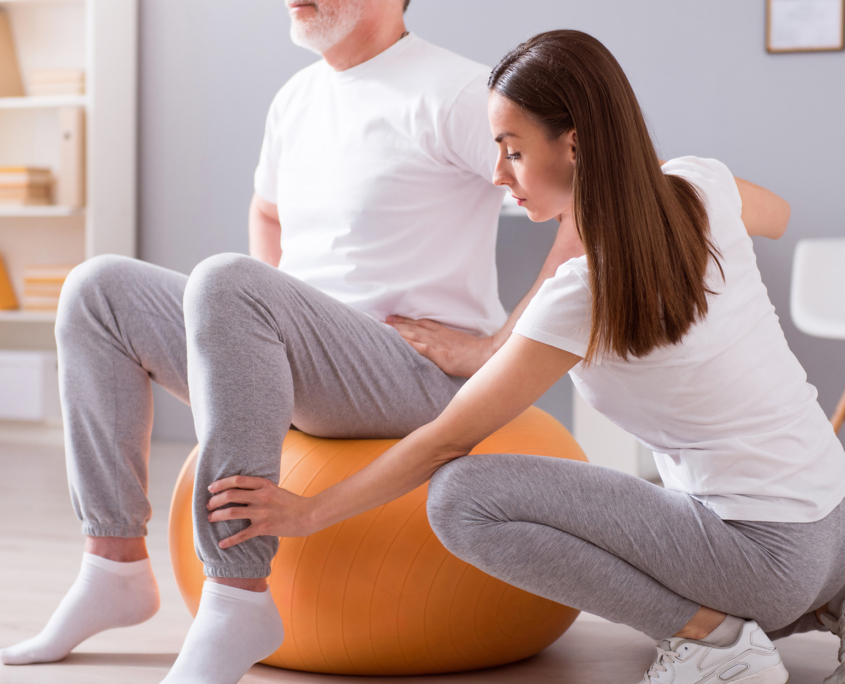 Female caregiver helping an older man work out on an exercise ball