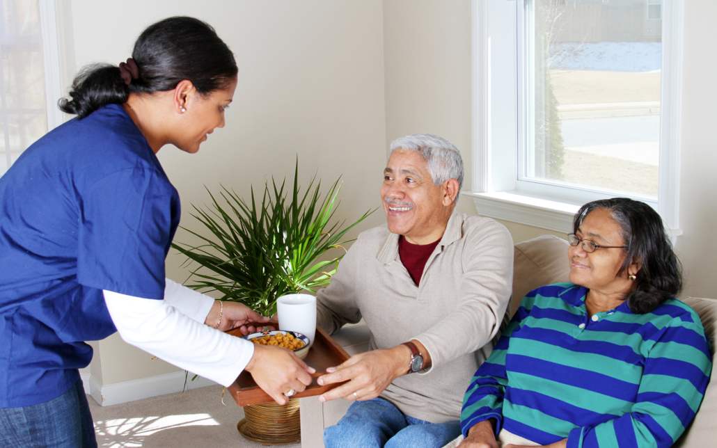 Female caregiver passing food to an older couple