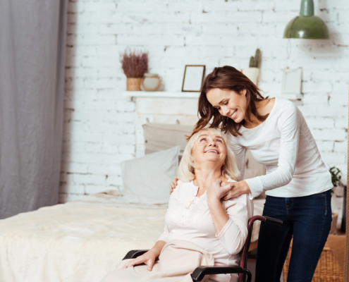 A young woman helping an older adult from bed into her wheelchair