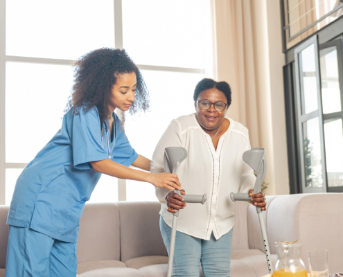 Female caregiver helps an older adult with her crutches