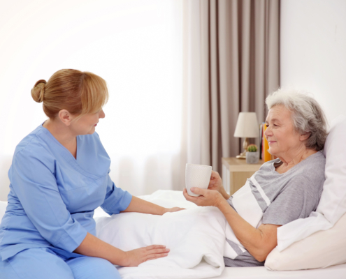 Female caregiver checking in with an elderly woman as she rests in her bed