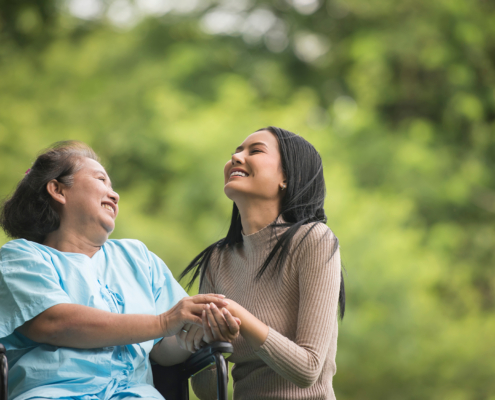 Young woman and an older woman in a wheelchair enjoying a walk through the park