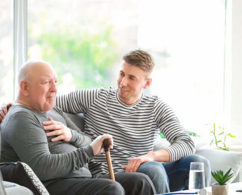 Male family caregiver having a conversation on the couch with an older relative