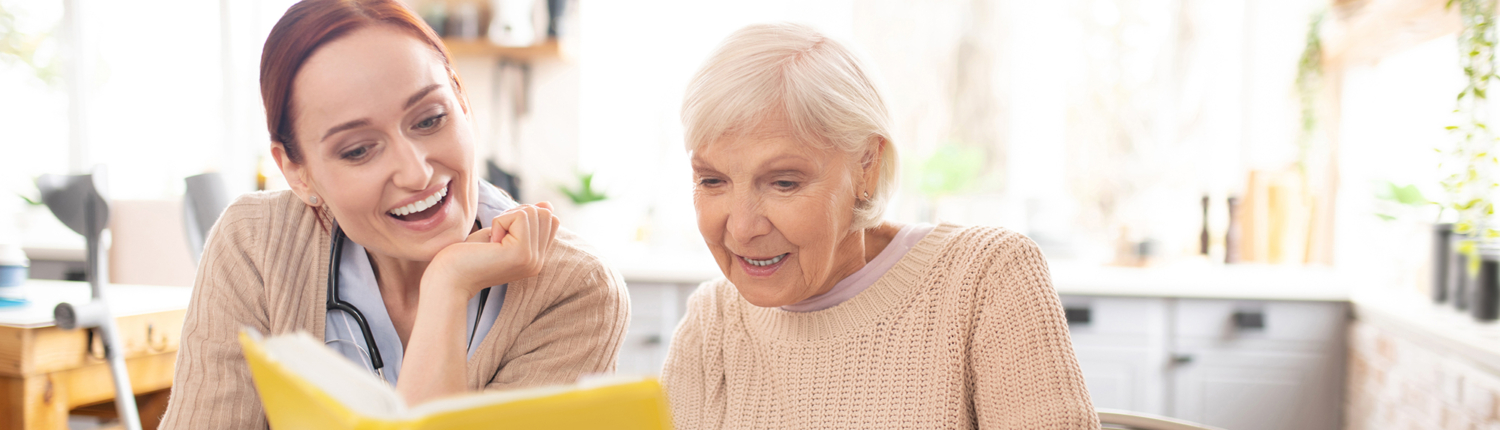 Female caregiver reading book with elderly woman