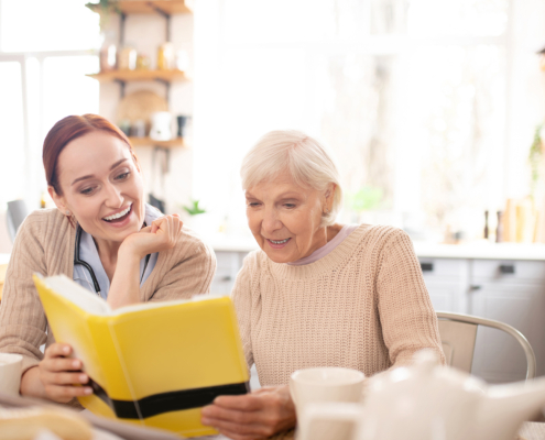 Female caregiver reading book with elderly woman